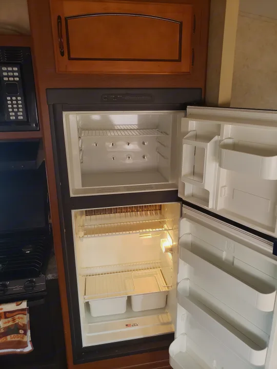 Interior of an RV rental showing an empty, open refrigerator, microwave, and stovetop in a clean kitchen area.. Keystone RV Springdale 2013