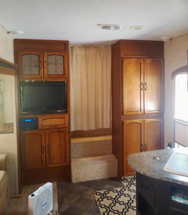 Cozy RV rental interior: kitchen counter, entertainment, and carpeted steps leading to a private area.. Keystone RV Springdale 2013