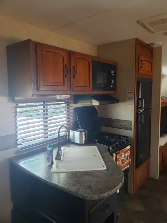 Compact RV rental kitchen with sink, stove, microwave, fridge, and toaster, ready for travel.. Keystone RV Springdale 2013