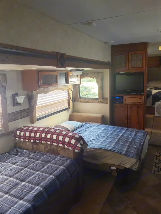 Cozy RV rental interior featuring two plaid sleeping areas, a TV, and window view; ideal for travel comfort.. Keystone RV Springdale 2013