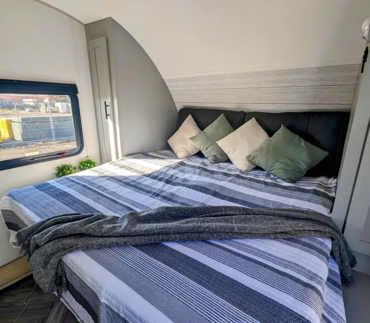 Spacious RV rental bedroom featuring a comfy bed with striped bedding, throw, and four pillows.. Forest River Wildwood FSX 2021