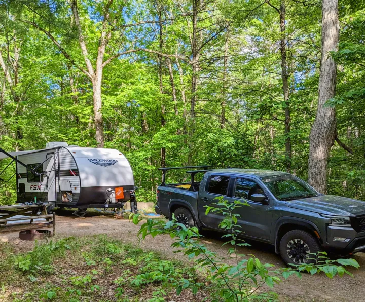 RV rental adventure: Pickup truck & Wildwood travel trailer parked at a serene wooded campsite with a picnic table.. Forest River Wildwood FSX 2021