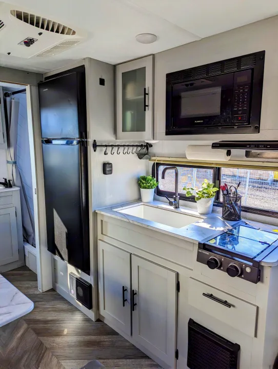 Modern RV rental kitchen featuring a sink, microwave, stovetop, and fridge, designed for comfortable travel living.. Forest River Wildwood FSX 2021