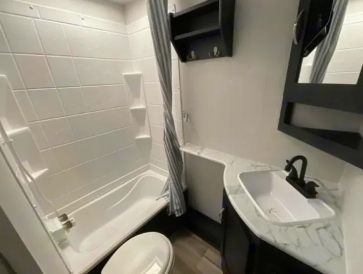 A well-lit, modern RV rental bathroom features a white tub/shower, toilet, and black vanity with white sink.. Coachmen Freedom Express Ultra Lite 238BHS 2022