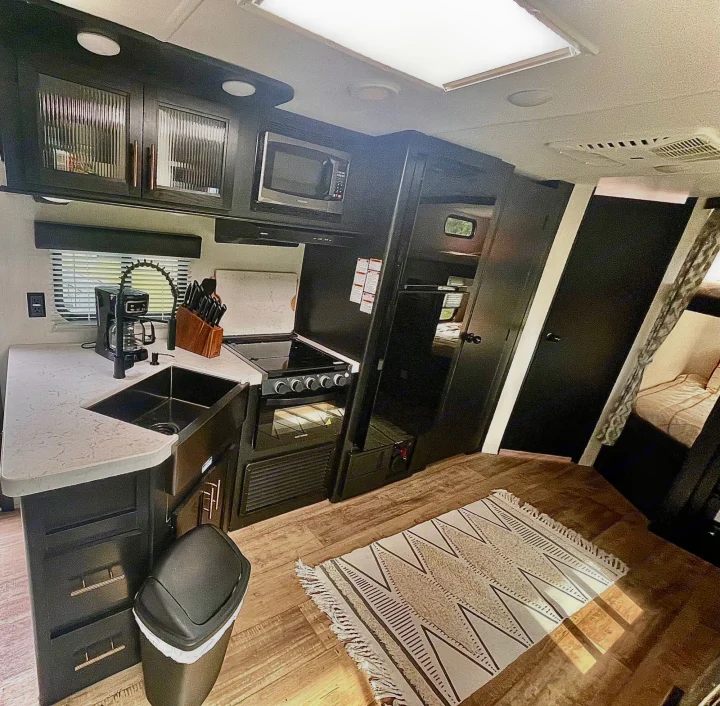 See this rv rental's sleek, modern kitchen: black cabinets, white counters, sink, stove, microwave, & wood floors.. Forest River Cherokee Grey Wolf 2022