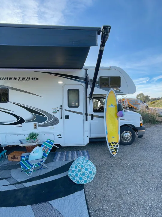 Our rv rental offers a perfect outdoor setup with an extended awning, chairs, a table, and a surfboard for camping fun.. Forest River Forester 2020