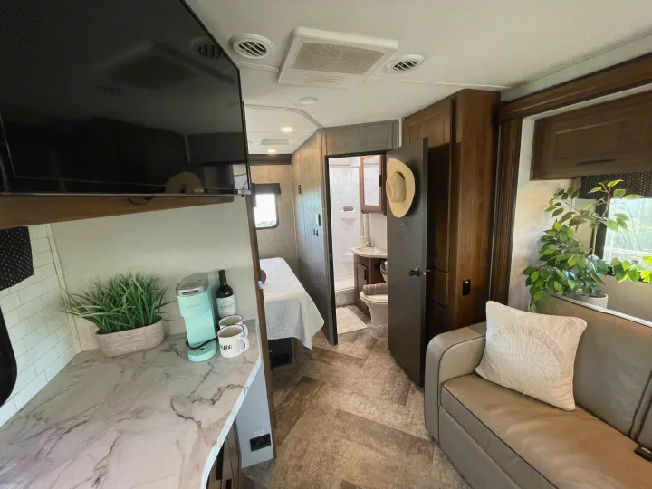 Step inside this inviting rv rental, showcasing its modern living room, kitchen counter, bed, and bathroom beyond.. Forest River Forester 2020