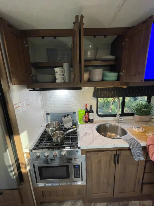 Modern rv rental kitchen with stove, built-in microwave, sink, spacious counter, and overhead cabinets for dishes.. Forest River Forester 2020