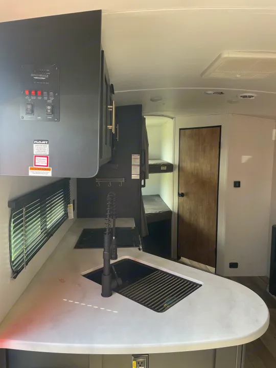 Inside an RV rental, featuring the kitchen with a sink, control panel, and bunk beds in the background.. Keystone RV Springdale 2022