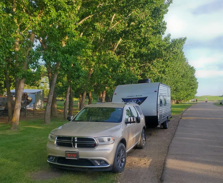 Beige Dodge Durango SUV with an RV rental (Forest River travel trailer) parked by trees on a dirt road, ready for adventure.. Forest River Salem FSX 2019