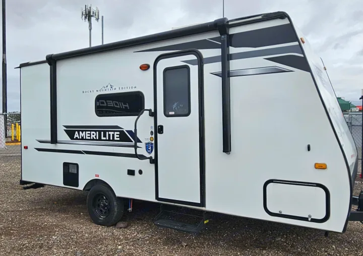 Side view of a white Ameri Lite travel trailer, a compact RV rental with its awning extended for shade.. Gulf Stream Ameri-Lite LE 2023
