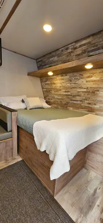 This RV rental offers a comfy bedroom with textured wood walls, shelf lighting, and a soft bed for a restful journey.. Gulf Stream Ameri-Lite LE 2023