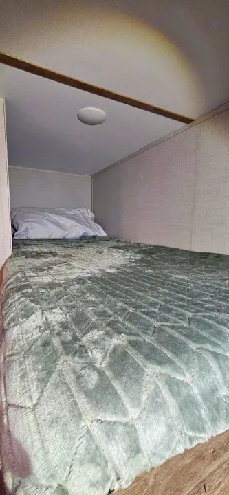Cozy RV rental bunk bed with a quilted green blanket and pillow, ideal for a compact sleeping space.. Gulf Stream Ameri-Lite LE 2023