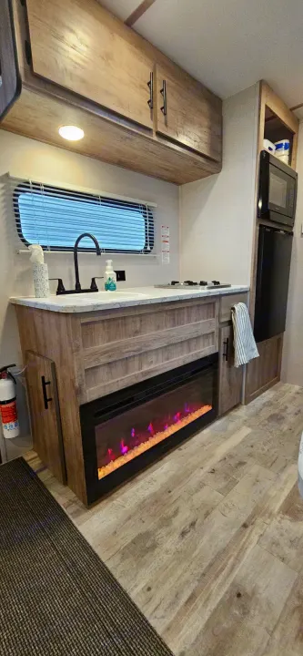 Modern RV rental interior with kitchen, sink, stove, microwave, fridge, and cozy electric fireplace under countertop.. Gulf Stream Ameri-Lite LE 2023