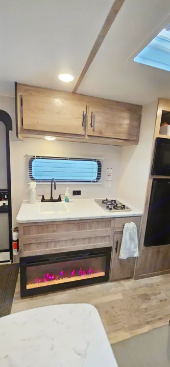 Well-appointed RV rental interior featuring a modern kitchen with sink, stove, and a comforting electric fireplace. Ideal for journeys.. Gulf Stream Ameri-Lite LE 2023