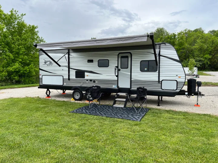 A Jayco Jay Flight travel trailer rv rental fully set up on a grassy campsite with awning, chairs, and mat.. Jayco Jay Flight SLX 2021