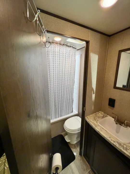 Inside an RV rental, a compact bathroom features a shower with a geometric curtain, toilet, sink, and vanity.. Jayco Jay Flight SLX 2021