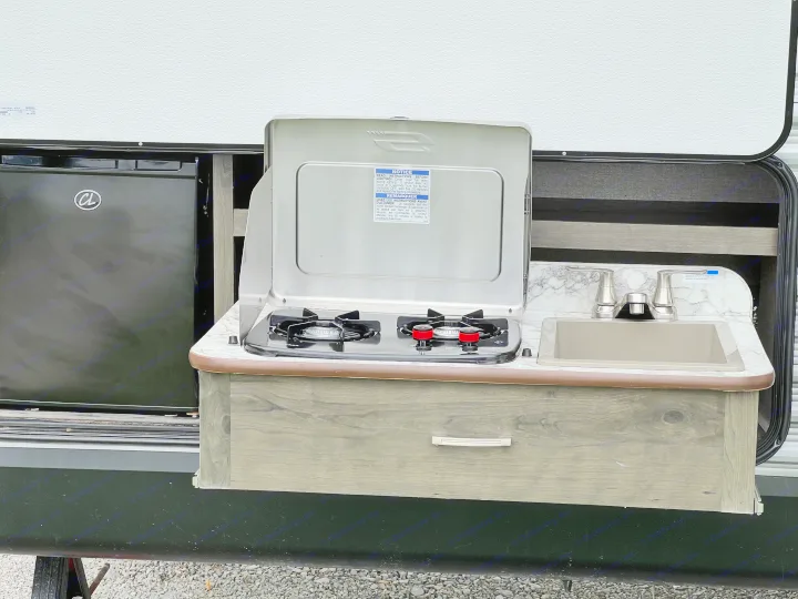 Modern RV rental outdoor kitchen with a compact fridge, two-burner propane stove, and sink for convenient camping trips.. Jayco Jay Flight SLX 2021