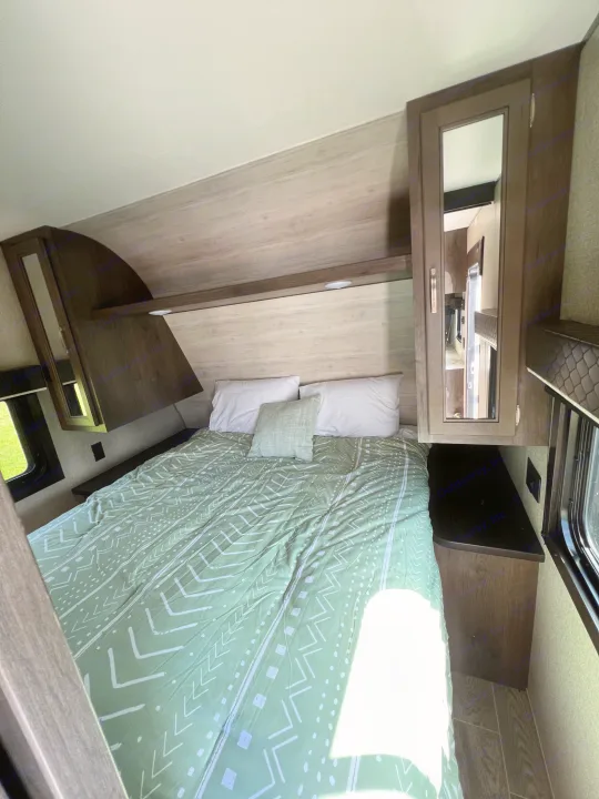 Cozy RV rental bedroom with a green patterned bed, ample storage, and mirrored cabinet. Modern and clean design.. Jayco Jay Flight SLX 2021