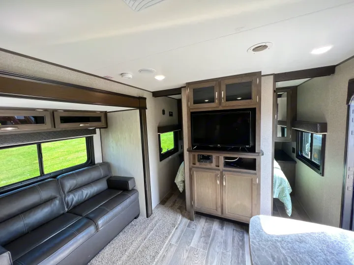 Inside an RV rental: a modern living space featuring a gray sofa, TV, cabinets, and light wood flooring.. Jayco Jay Flight SLX 2021