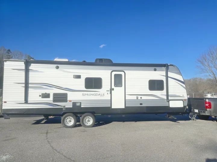 This white and black travel trailer, an RV rental option, is hitched to a pickup truck on a clear day.. Keystone RV Springdale 2020