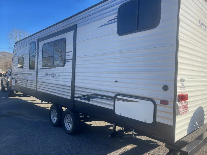 This large silver Springdale travel trailer, perfect for an rv rental, is parked outdoors. Features windows and tandem axles.. Keystone RV Springdale 2020