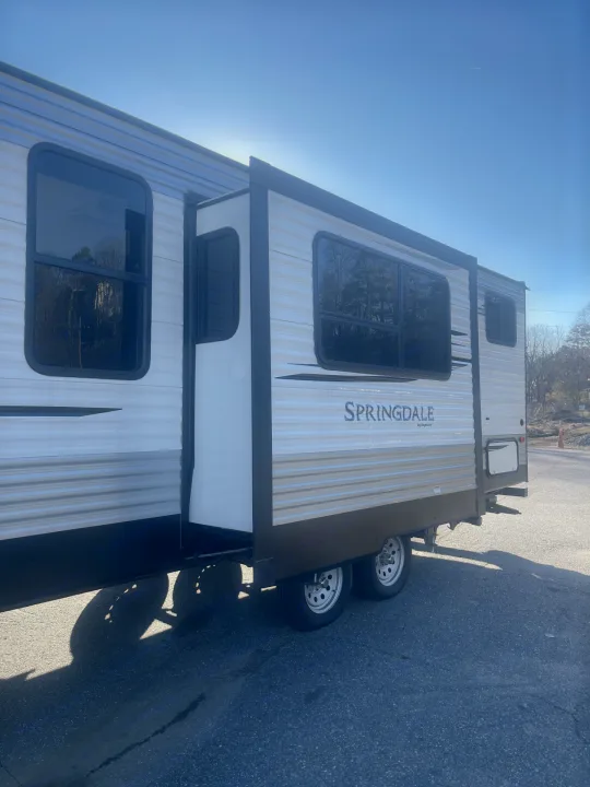White Springdale travel trailer with an extended slide-out, parked on asphalt under a clear blue sky.. Keystone RV Springdale 2020