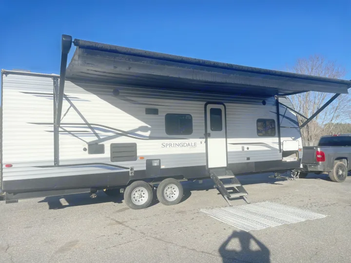 Extended awning on a Springdale RV rental, hitched to a truck. Parked on asphalt, ready for outdoor recreation.. Keystone RV Springdale 2020
