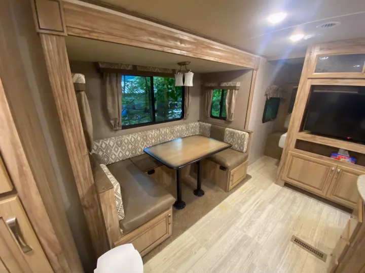 Spacious RV rental interior with U-shaped dinette, large windows showing foliage, and an entertainment unit. Perfect for mobile living.. Palomino 240bhs 2018