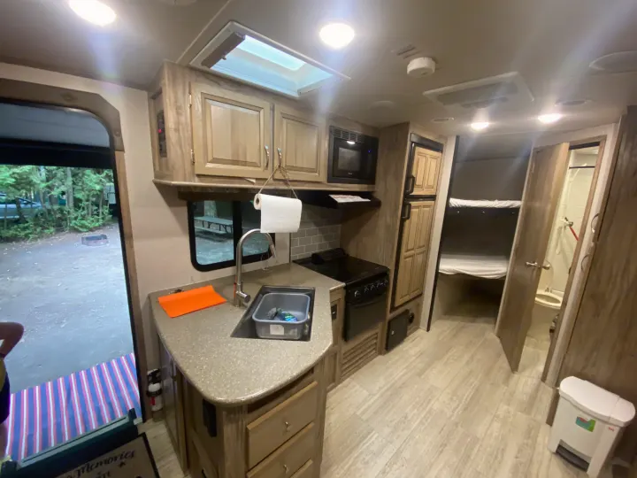 Spacious RV rental interior with kitchen, bunk beds, and view of a campsite.. Palomino 240bhs 2018