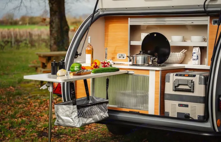 An RV rental's open rear hatch shows a compact outdoor kitchen: stove, sink, fresh produce, and a cooler. Ready for travel!. Caretta 1500 2024