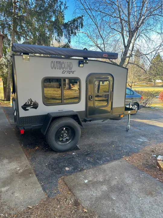 A rugged Outbound Extreme camper trailer, an excellent RV rental choice for outdoor adventures, parked on a driveway.. Outbound Extreme 2021