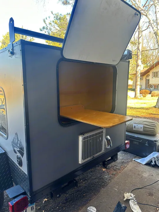 Open rear galley on a compact **RV rental** teardrop trailer, ready for camping trips. Features wood counter, cooler, & roof rack.. Outbound Extreme 2021