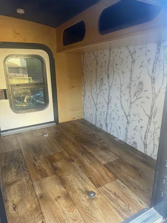 Cozy RV rental interior with wood-look floor, owl wallpaper, and light wood panels, perfect for your next adventure.. Outbound Extreme 2021