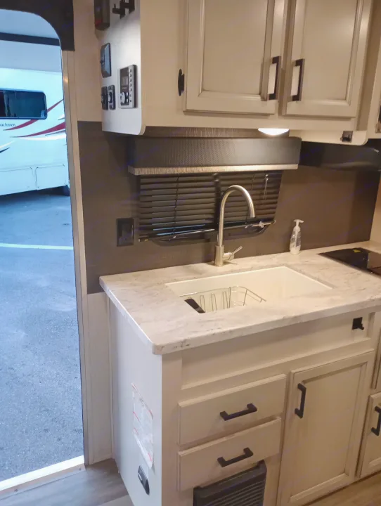 This RV rental's kitchen features a modern sink, light countertops, and stylish cabinets. See the outside through the open door.. Highland Ridge RV Open Range 2022
