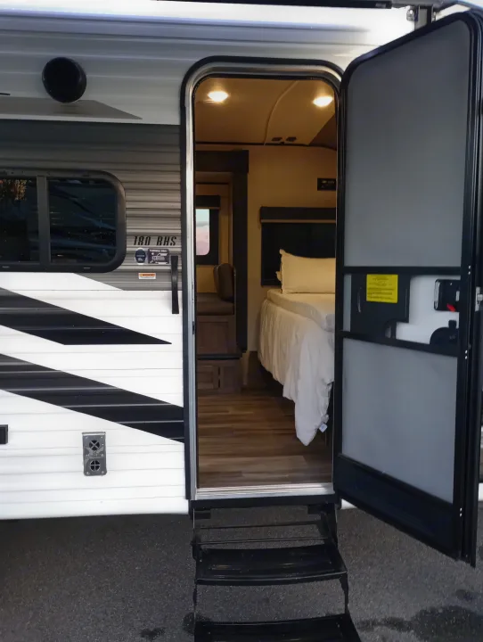 Experience an RV rental! This photo shows the open side door of a travel trailer, revealing its inviting interior bedroom and steps.. Highland Ridge RV Open Range 2022