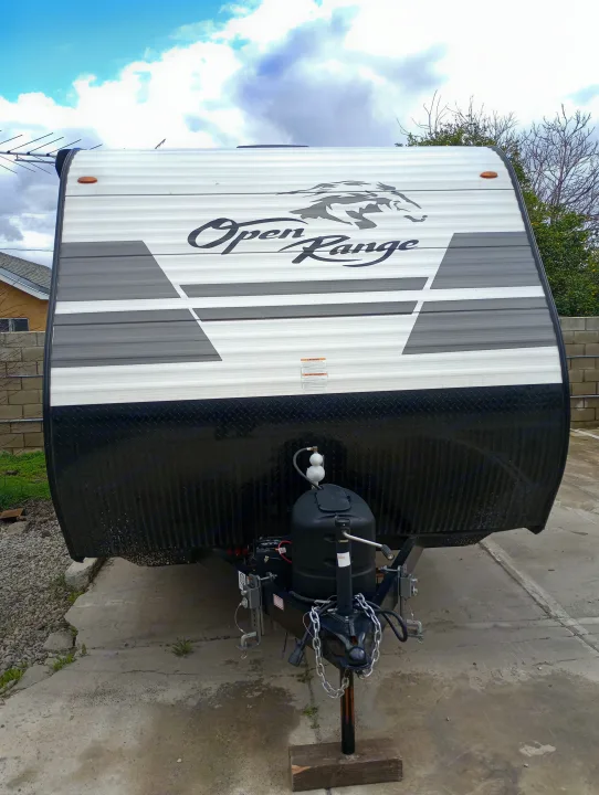 Front view of a white travel trailer with black diamond plate, ready for an RV rental. Visible are propane tanks & hitch.. Highland Ridge RV Open Range 2022