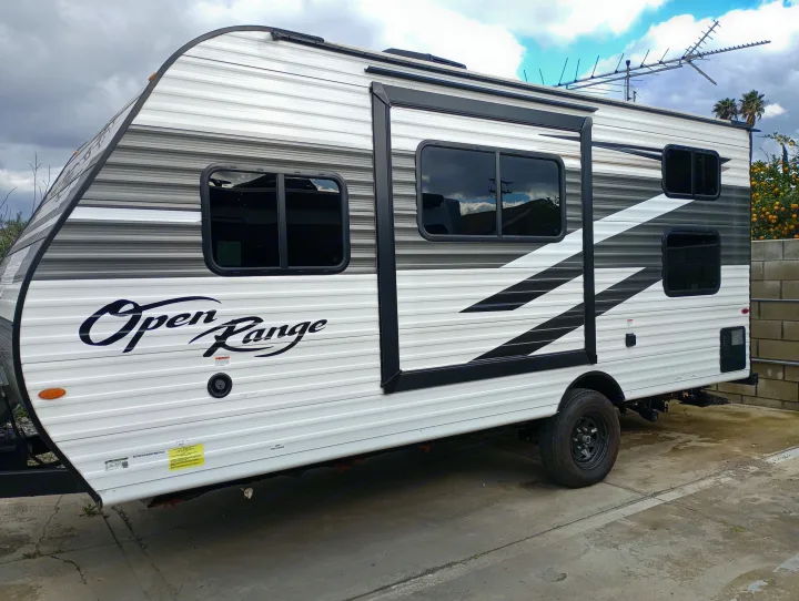 A white and gray Open Range travel trailer, a modern RV, is parked on concrete. Ideal for an upcoming RV rental journey.. Highland Ridge RV Open Range 2022
