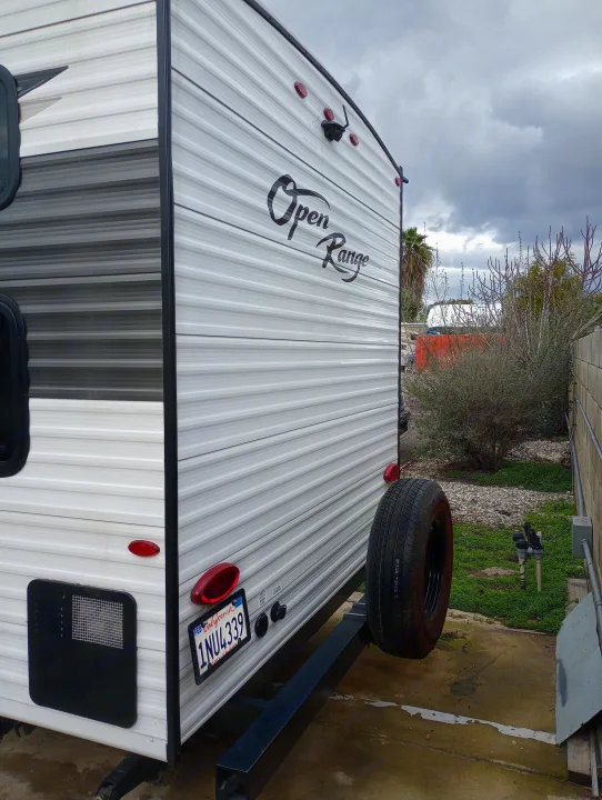 Open Range travel trailer (RV rental option) parked outdoors. Rear view shows spare tire, California plate 1NU4339.. Highland Ridge RV Open Range 2022
