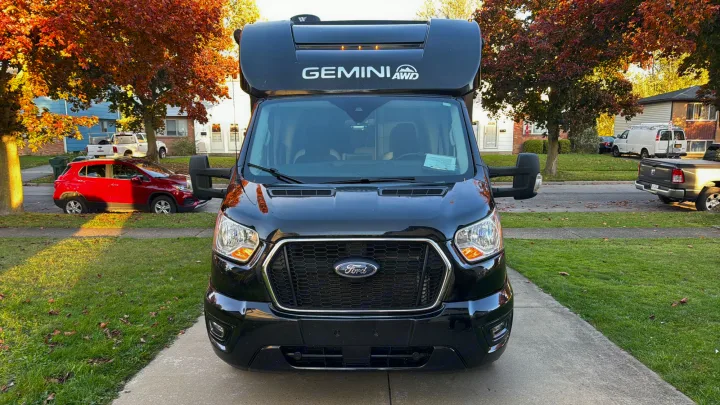Black Ford Gemini AWD RV rental parked on a driveway, front view. Residential street scene with autumn trees.. Thor Gemini 2022