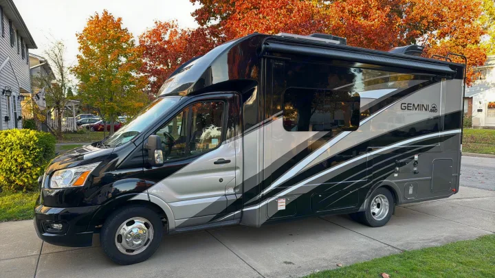 Sleek black & silver Thor Gemini AWD Class C RV rental parked on a driveway, with autumn trees.. Thor Gemini 2022