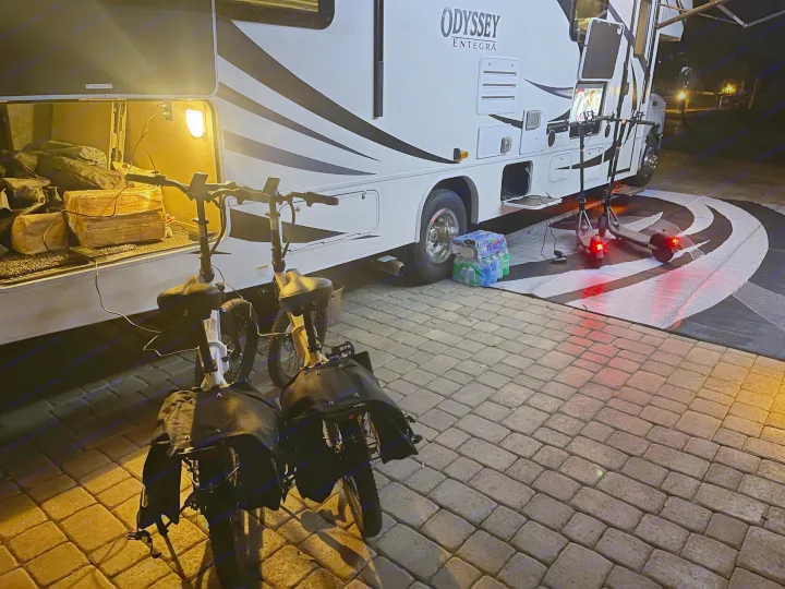 Nighttime RV rental: An Odyssey Entegra motorhome with electric bikes and scooters charging on a paved campsite.. Entegra Coach Odyssey 2020