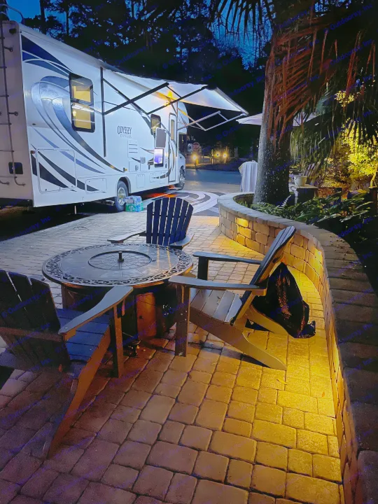Relaxing night at an RV rental site. Illuminated patio with fire pit, chairs, and an extended awning on an Odyssey Entegra RV.. Entegra Coach Odyssey 2020