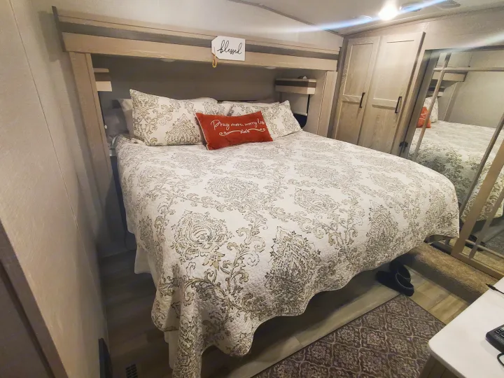 Cozy RV rental bedroom features a patterned bed, built-in storage, and mirrored wardrobe for comfortable travel.. Forest River Rockwood Ultra Lite 2022