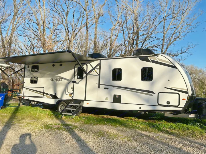 Experience the outdoors with this spacious white RV rental, a Sunset Trail travel trailer parked under bare trees on a sunny day.. Crossroads RV Sunset Trail 2022
