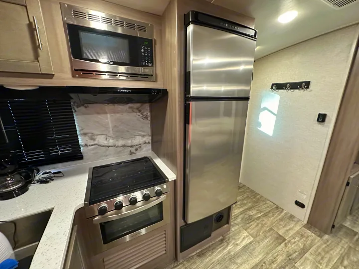 Step inside this modern **rv rental** kitchen, featuring a stainless steel microwave, Furrion range hood, Greystone stove/oven, fridge, and sink.. Crossroads RV Sunset Trail 2022
