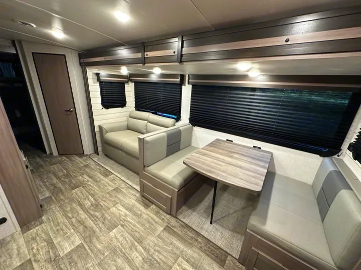 Modern RV rental interior with light wood flooring, grey sofa, and a dinette booth with a light wooden table. Inviting living space.. Crossroads RV Sunset Trail 2022