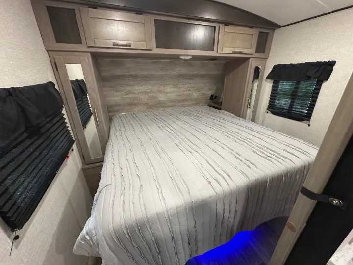 RV rental bedroom: a large bed, overhead storage, mirrored wardrobes, window blinds, and blue ambient light.. Crossroads RV Sunset Trail 2022