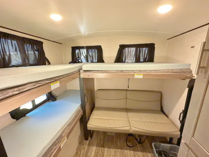 Spacious RV rental interior featuring comfortable bunk beds, a lower sofa, and black-out window curtains. Ideal for family travel.. Crossroads RV Sunset Trail 2022