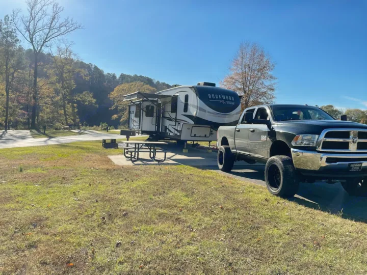 This RV rental is ready for adventure! A black truck tows a Rockwood fifth-wheel at a sunlit campsite.. Forest River Rockwood Ultra Lite 2022